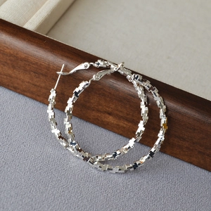 Macro shot of silver hoop earrings featuring geometric faceted blocks and metal texture