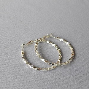Detailed macro view of large silver hoop earrings featuring geometric faceted texture