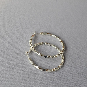 Detailed macro view of silver hoop earrings featuring a unique textured mosaic surface