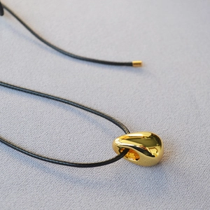 Close-up of a polished gold water-drop pendant on a black cord over purple fabric