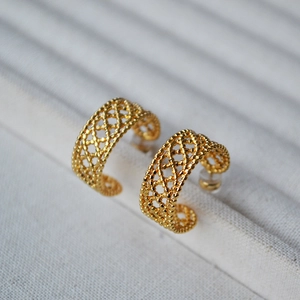 Detailed macro view of gold-plated C-shaped earrings with intricate woven lace texture