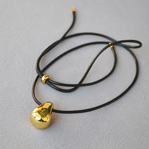 Detailed macro view of golden teardrop pendant with black adjustable cord necklace
