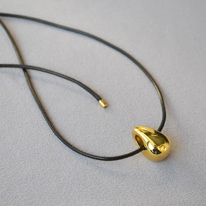 Macro detail of golden teardrop pendant on black woven cord with mirror finish
