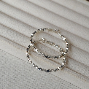Detailed macro view of large silver hoop earrings featuring a sparkling textured surface