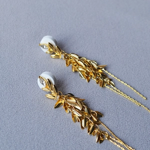 Détail de boucles d'oreilles pampilles feuilles dorées avec cristaux et clous en argent