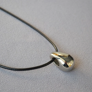 Close-up of minimalist silver teardrop pendant with black leather cord on gray background
