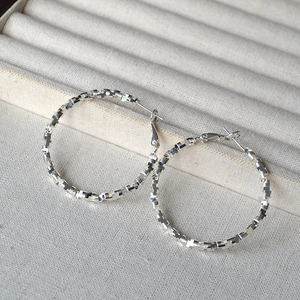 Close-up of silver geometric hoop earrings with textured pixelated surface on velvet