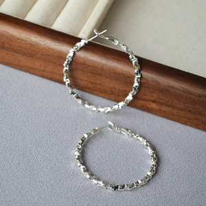 Detailed view of silver hoop earrings with irregular faceted texture on a jewelry box