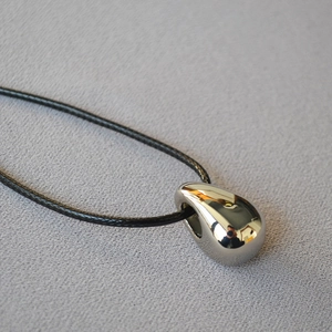 Detailed view of silver teardrop pendant with reflective finish on black cord necklace