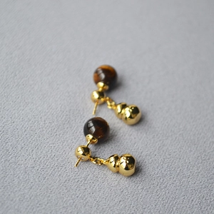 Detail of tiger eye stone bead and golden metal gourd drop earrings on a grey background