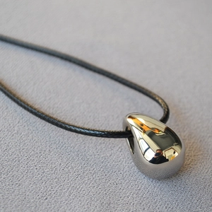 Macro shot of mirror-polished silver teardrop pendant on a black cord necklace