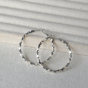 Minimalist silver hoop earrings with a textured sparkling surface on a soft beige fabric