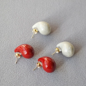 Macro detail of red enamel and white pearl drop earrings with gold needles on fabric