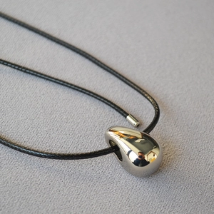 Detailed view of a polished silver teardrop pendant on a black braided leather cord