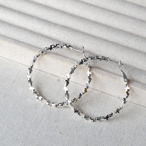 Detailed view of silver hoop earrings featuring a unique textured cross-shaped geometric design