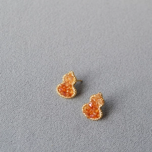 Macro detail of gourd-shaped studs with orange crystal inlay and gold finish