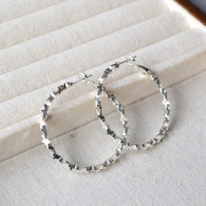 Macro detail of silver faceted hoop earrings with shimmering irregular texture