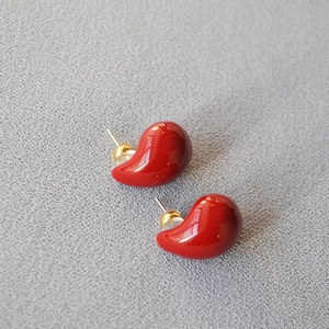 Close-up of handmade red enamel teardrop stud earrings with gold pins on fabric