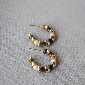 Detail of C-shaped tiger eye stone beaded earrings with silver needles on gray fabric