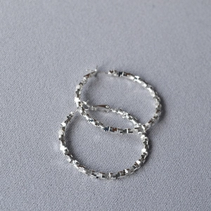 Macro detail of silver hoop earrings featuring geometric faceted texture and polished finish