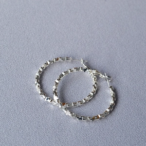Macro detail of silver irregular hoop earrings with faceted mosaic texture surface