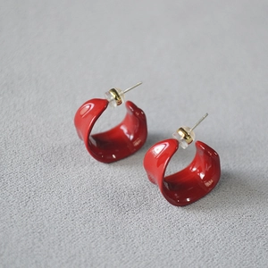 Detailed view of red enamel twisted C-shape earrings with gold studs on gray surface