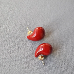 Detail of red enamel water drop stud earrings with gold pins on textured background