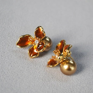 Macro detail of vintage floral earrings with orange enamel, zircon, and golden pearl