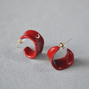 Macro view of red enamel irregular C-shape stud earrings with silver pins and secure backs