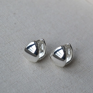 Detail of silver polished geometric triangle hoop earrings on soft textured background