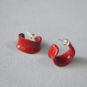 Macro shot of bright red enamel C-shaped earrings with glossy finish and silver needles