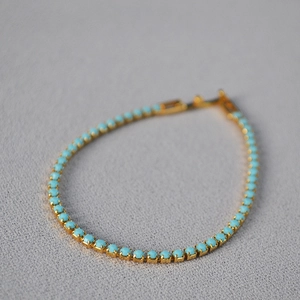 Detail of minimalist gold-plated tennis bracelet featuring turquoise blue beads and clasp