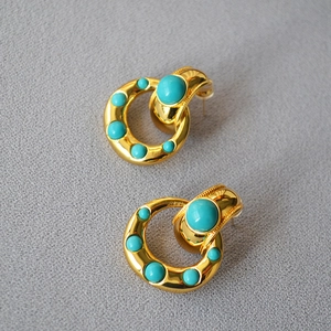 Vintage style gold-plated brass earrings set with round turquoise stones on fabric background