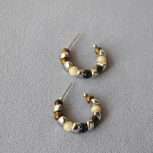 Macro detail of C-shaped silver beaded earrings with tiger eye and mineral stones