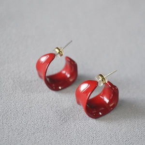 Macro detail of red enamel C-shaped earrings with irregular wavy edges and gold posts