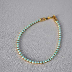 Elegant gold tennis bracelet with round turquoise stones and a secure clasp on gray fabric
