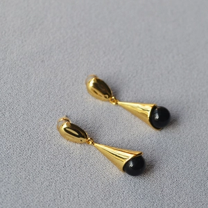 Detailed side view of long gold drop earrings with black agate beads on grey fabric