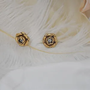 Macro shot of vintage gold rose stud earrings with diamond inlay on white feathers