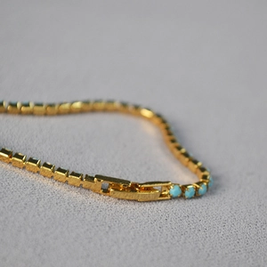 Detailed close-up of blue turquoise beads on gold chain with secure folding clasp