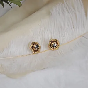 Vintage 3D carved gold rose earrings with crystal center on a white feather background