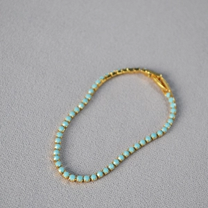 Detailed view of a gold tennis bracelet with light blue turquoise beads and clasp