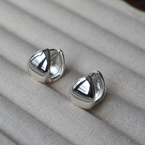 Macro shot of mirror-polished gold drop earrings on a beige textured jewelry tray