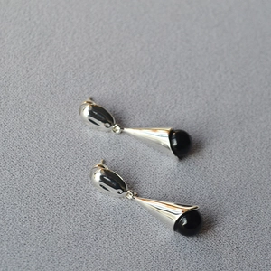 Close-up of long teardrop earrings with silver finish and black onyx stone beads