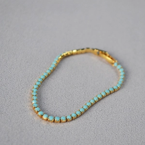 Detailed macro view of a gold-plated turquoise tennis bracelet with fold-over clasp
