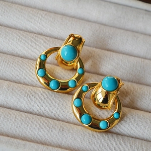 Detailed shot of vintage gold brass earrings with turquoise stones on soft beige velvet