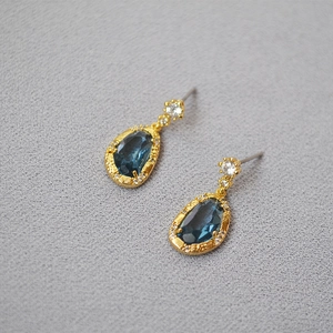 Macro detail of pear-shaped sapphire blue crystal earrings with gold finish and zircons