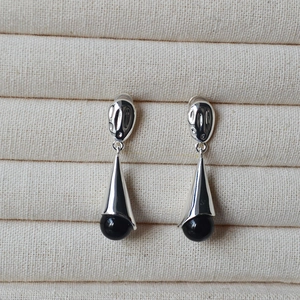 Detail of silver drop earrings with sleek metal cone and polished black onyx beads