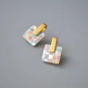 Close-up of square shell mosaic earrings with iridescent shell and matte gold accents