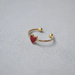 Macro shot of gold-plated open ring with a red enamel heart on a grey fabric background