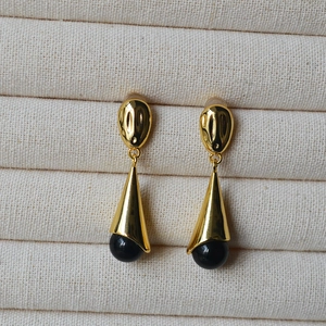 Close-up of long teardrop earrings with gold plating and black onyx on a beige tray
